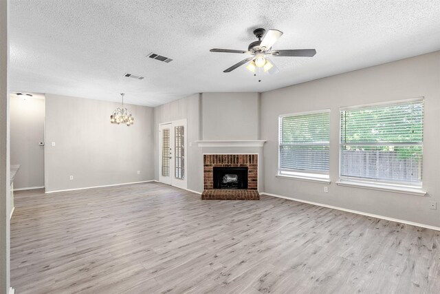 unfurnished living room with a textured ceiling, a brick fireplace, a healthy amount of sunlight, and light hardwood / wood-style flooring