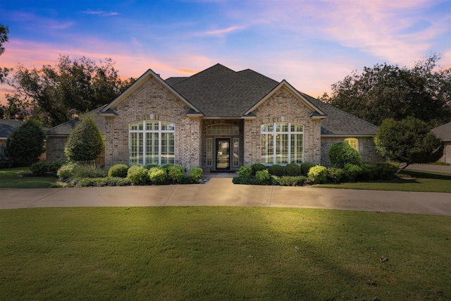 view of front of home featuring roof with shingles, brick siding, and a front lawn