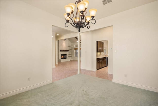 unfurnished dining area with a large fireplace, baseboards, visible vents, and light colored carpet