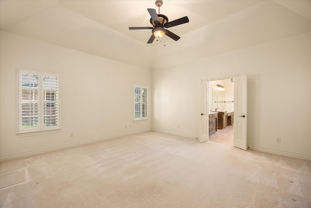 unfurnished bedroom with light colored carpet, connected bathroom, baseboards, and ceiling fan