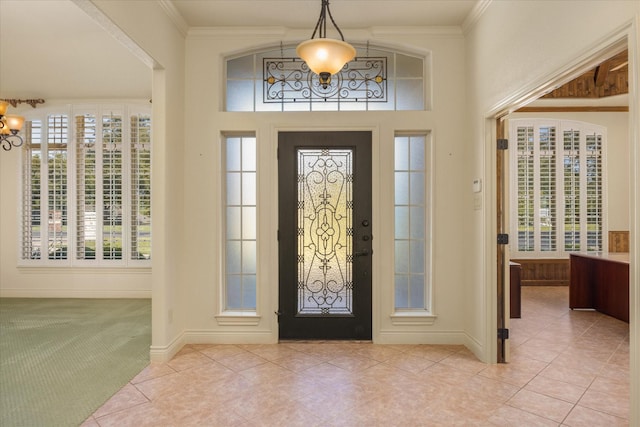 entryway with light carpet, ornamental molding, a notable chandelier, and baseboards