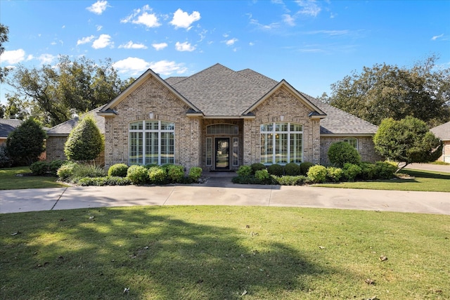 view of front of home with roof with shingles, a front yard, and brick siding