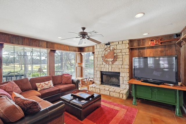 tiled living room featuring a fireplace, ceiling fan, wood walls, and a textured ceiling