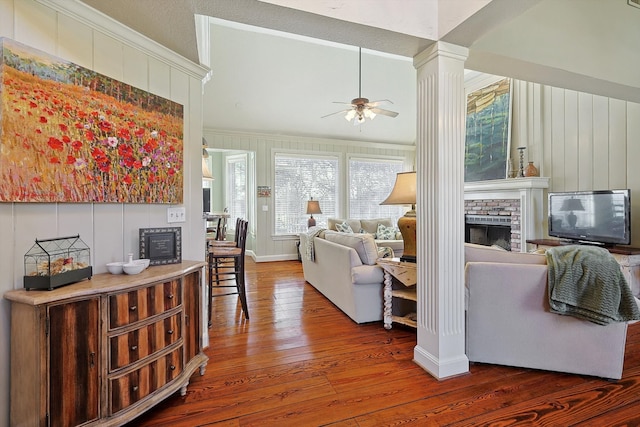 living room featuring ceiling fan, ornamental molding, wood-type flooring, a fireplace, and ornate columns