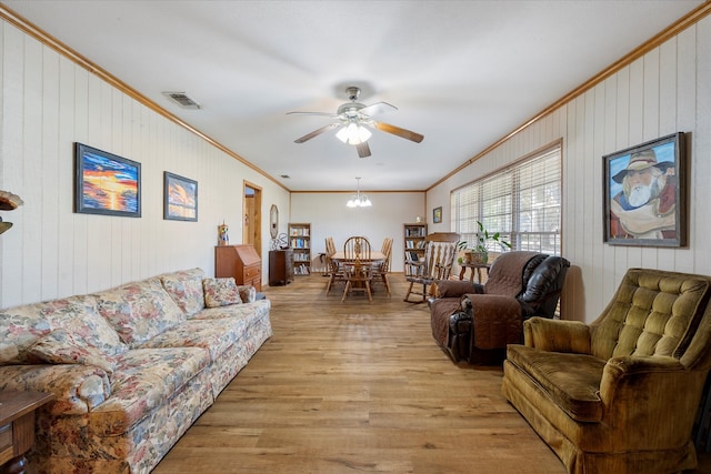 living room with crown molding, ceiling fan with notable chandelier, light hardwood / wood-style floors, and wooden walls