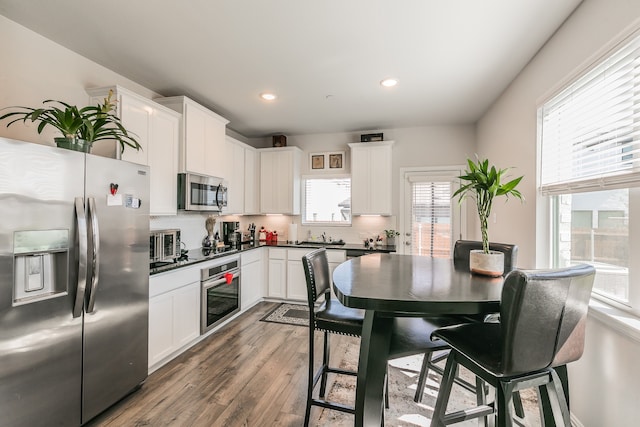 kitchen with backsplash, white cabinetry, hardwood / wood-style floors, and stainless steel appliances