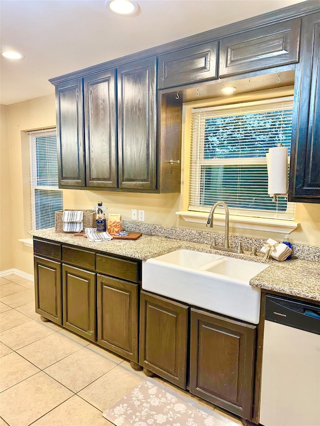 kitchen with light tile patterned flooring, dishwashing machine, sink, and light stone counters