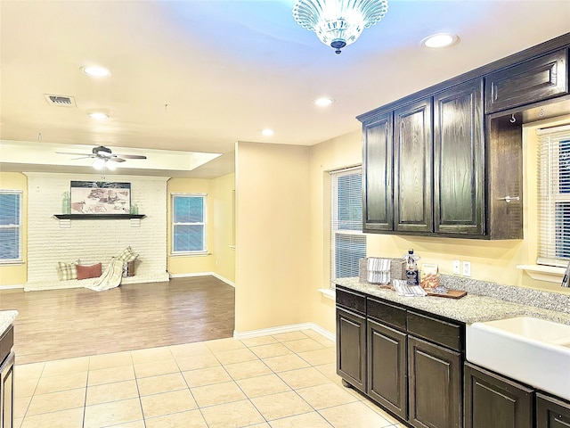 kitchen with light stone counters, sink, light wood-type flooring, and ceiling fan with notable chandelier