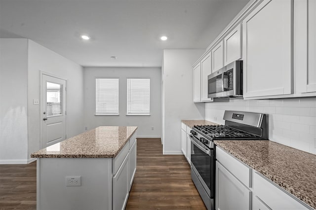 kitchen with light stone counters, a kitchen island, white cabinetry, appliances with stainless steel finishes, and dark hardwood / wood-style flooring