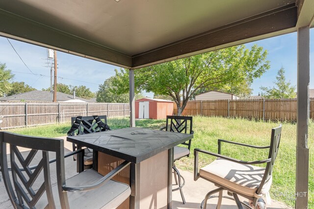view of patio / terrace with an outbuilding, a fenced backyard, outdoor dining space, and a storage unit