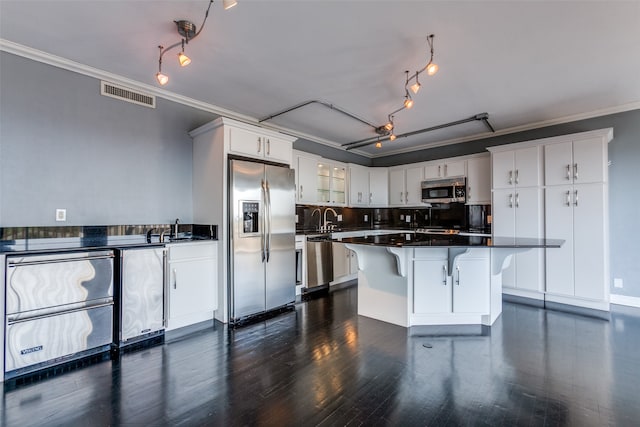 kitchen with dark hardwood / wood-style floors, a kitchen breakfast bar, crown molding, white cabinetry, and appliances with stainless steel finishes