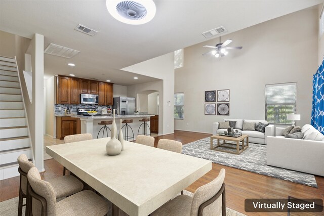 kitchen with appliances with stainless steel finishes, light wood-type flooring, ceiling fan, decorative backsplash, and a kitchen island with sink