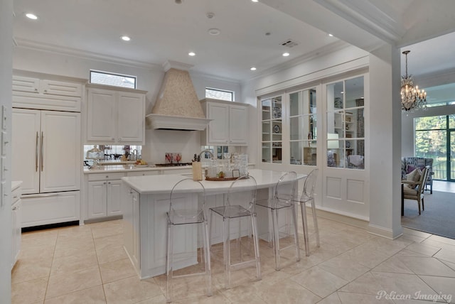 kitchen with a center island with sink, a notable chandelier, paneled built in fridge, hanging light fixtures, and custom exhaust hood