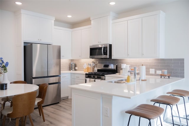 kitchen featuring white cabinets, sink, light hardwood / wood-style floors, a kitchen bar, and stainless steel appliances