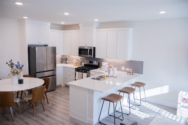 kitchen featuring white cabinetry, sink, stainless steel appliances, light hardwood / wood-style flooring, and a breakfast bar