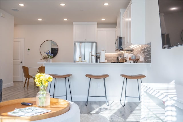 kitchen featuring decorative backsplash, white cabinets, stainless steel appliances, and light hardwood / wood-style floors