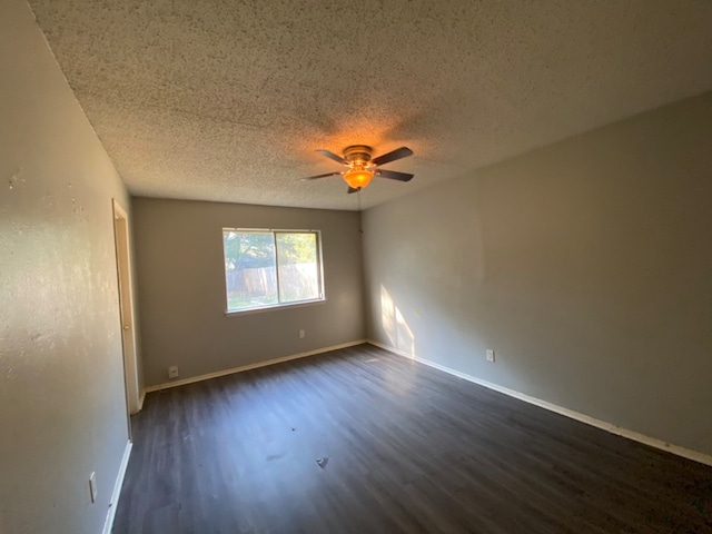 empty room with ceiling fan, dark hardwood / wood-style floors, and a textured ceiling