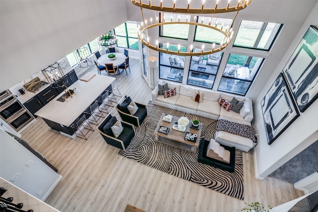 living room with a towering ceiling, a notable chandelier, a wealth of natural light, and hardwood / wood-style floors