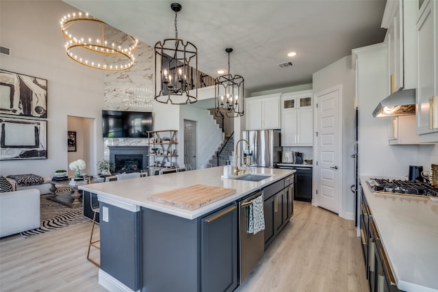 kitchen with a kitchen island with sink, sink, hanging light fixtures, exhaust hood, and white cabinetry