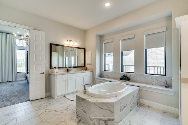 bathroom with vanity, a relaxing tiled tub, an inviting chandelier, and a wealth of natural light