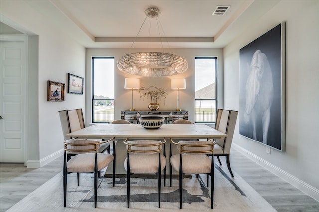 dining room with light wood-type flooring, a wealth of natural light, and a tray ceiling