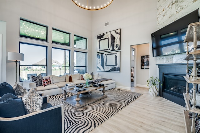 living room featuring a large fireplace, light hardwood / wood-style floors, a chandelier, and a towering ceiling