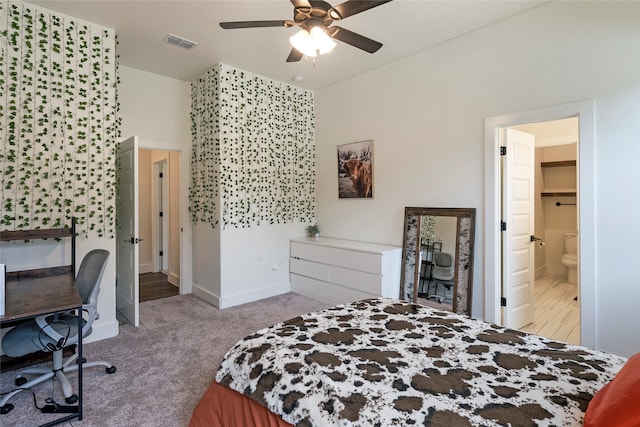 bedroom with ceiling fan, light colored carpet, and ensuite bath