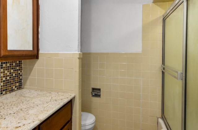 bathroom with an enclosed shower, tile walls, vanity, and toilet