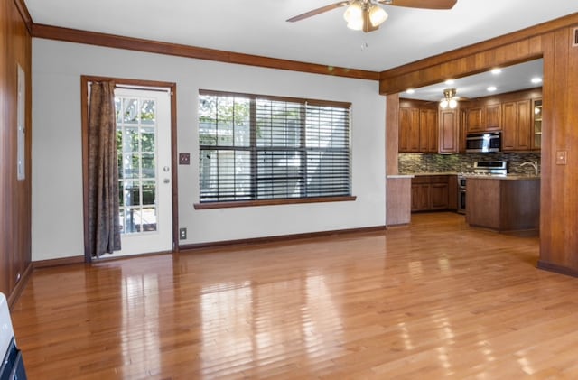 unfurnished living room with ceiling fan, sink, light wood-type flooring, and ornamental molding