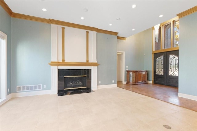 unfurnished living room with french doors, ornamental molding, and a tiled fireplace