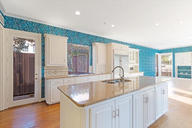 kitchen with appliances with stainless steel finishes, sink, white cabinets, a kitchen island with sink, and light stone countertops