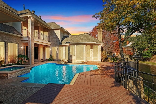 pool at dusk featuring an in ground hot tub and a wooden deck