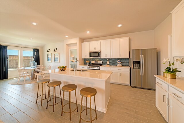 kitchen featuring sink, an island with sink, a breakfast bar, white cabinetry, and appliances with stainless steel finishes