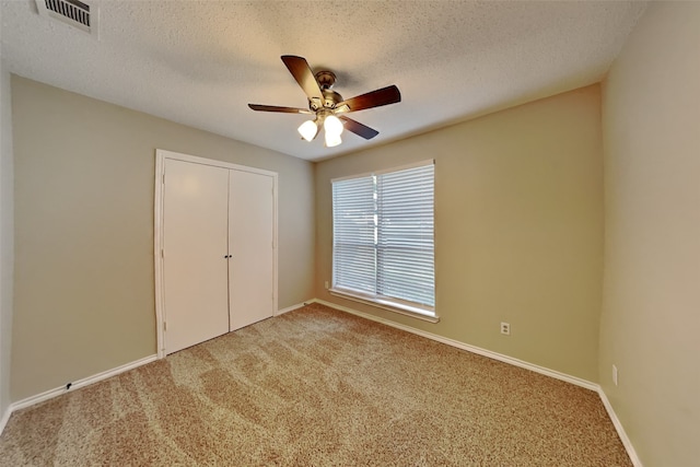 unfurnished bedroom with ceiling fan, light colored carpet, a textured ceiling, and a closet