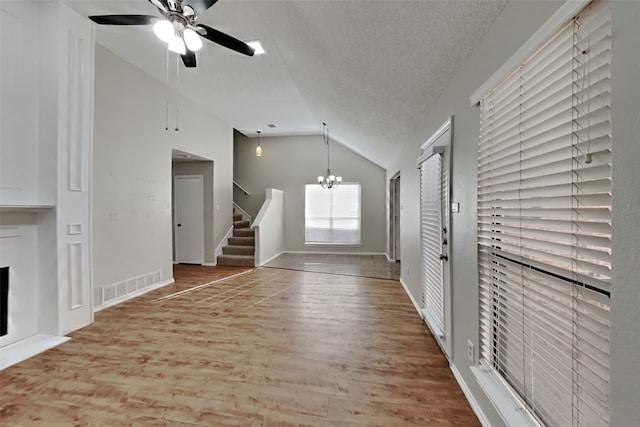 unfurnished living room with hardwood / wood-style flooring, ceiling fan with notable chandelier, vaulted ceiling, and a textured ceiling