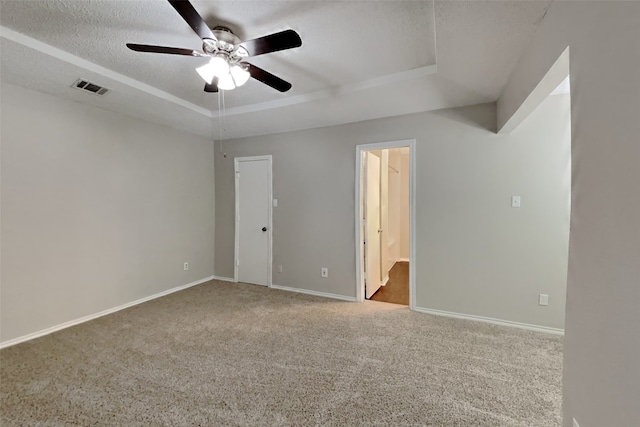 unfurnished room featuring a raised ceiling, light colored carpet, a textured ceiling, and ceiling fan