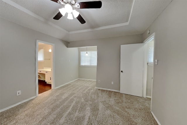 unfurnished bedroom featuring ceiling fan, a raised ceiling, a textured ceiling, carpet, and ensuite bath