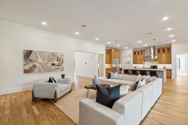 kitchen with pendant lighting, wall chimney exhaust hood, a large island with sink, and light hardwood / wood-style flooring