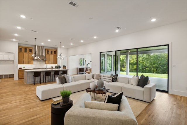 kitchen with built in fridge, a large island, pendant lighting, light hardwood / wood-style floors, and wall chimney exhaust hood