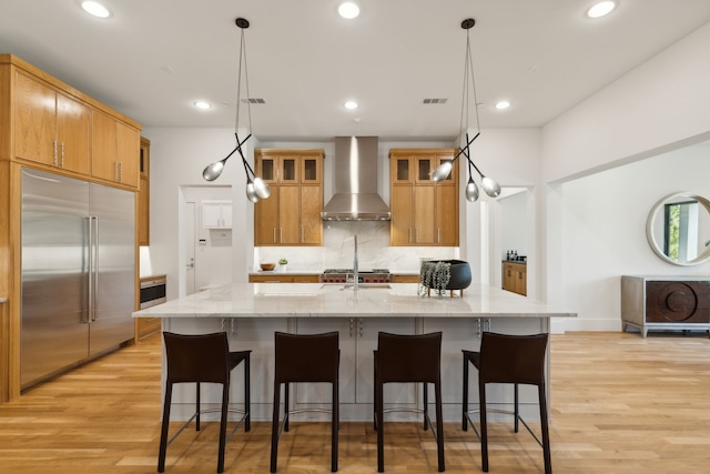 kitchen with premium appliances, light stone counters, wall chimney exhaust hood, and hanging light fixtures