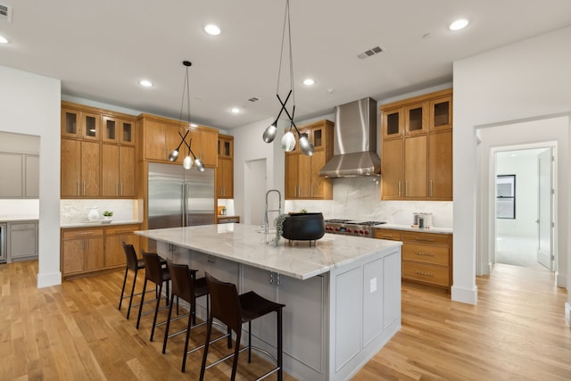 kitchen featuring light stone counters, a stone fireplace, light wood-type flooring, gray cabinets, and an island with sink