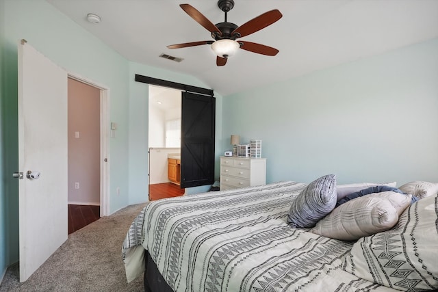 carpeted bedroom with ensuite bathroom, lofted ceiling, ceiling fan, and a barn door