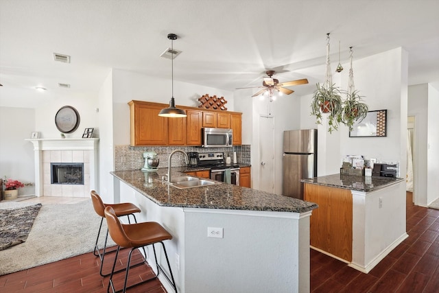 kitchen featuring a tiled fireplace, decorative light fixtures, stainless steel appliances, kitchen peninsula, and dark hardwood / wood-style floors