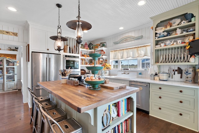 kitchen with pendant lighting, butcher block countertops, appliances with stainless steel finishes, a center island, and a kitchen bar