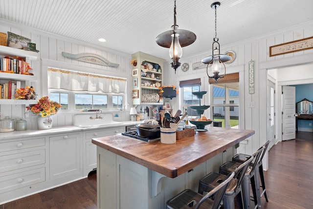 kitchen featuring pendant lighting, wooden counters, a kitchen island, white cabinetry, and a kitchen bar