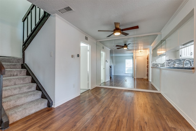 unfurnished living room featuring ceiling fan, sink, hardwood / wood-style flooring, a textured ceiling, and ornamental molding