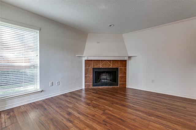 unfurnished living room featuring a tiled fireplace, dark hardwood / wood-style flooring, crown molding, and a textured ceiling