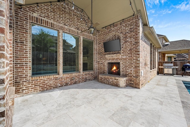 view of patio featuring area for grilling, ceiling fan, and an outdoor brick fireplace