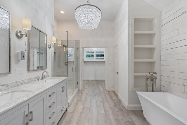 full bath featuring built in shelves, a stall shower, a sink, wood finished floors, and a freestanding tub