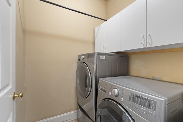 clothes washing area with washer and clothes dryer, cabinet space, and baseboards